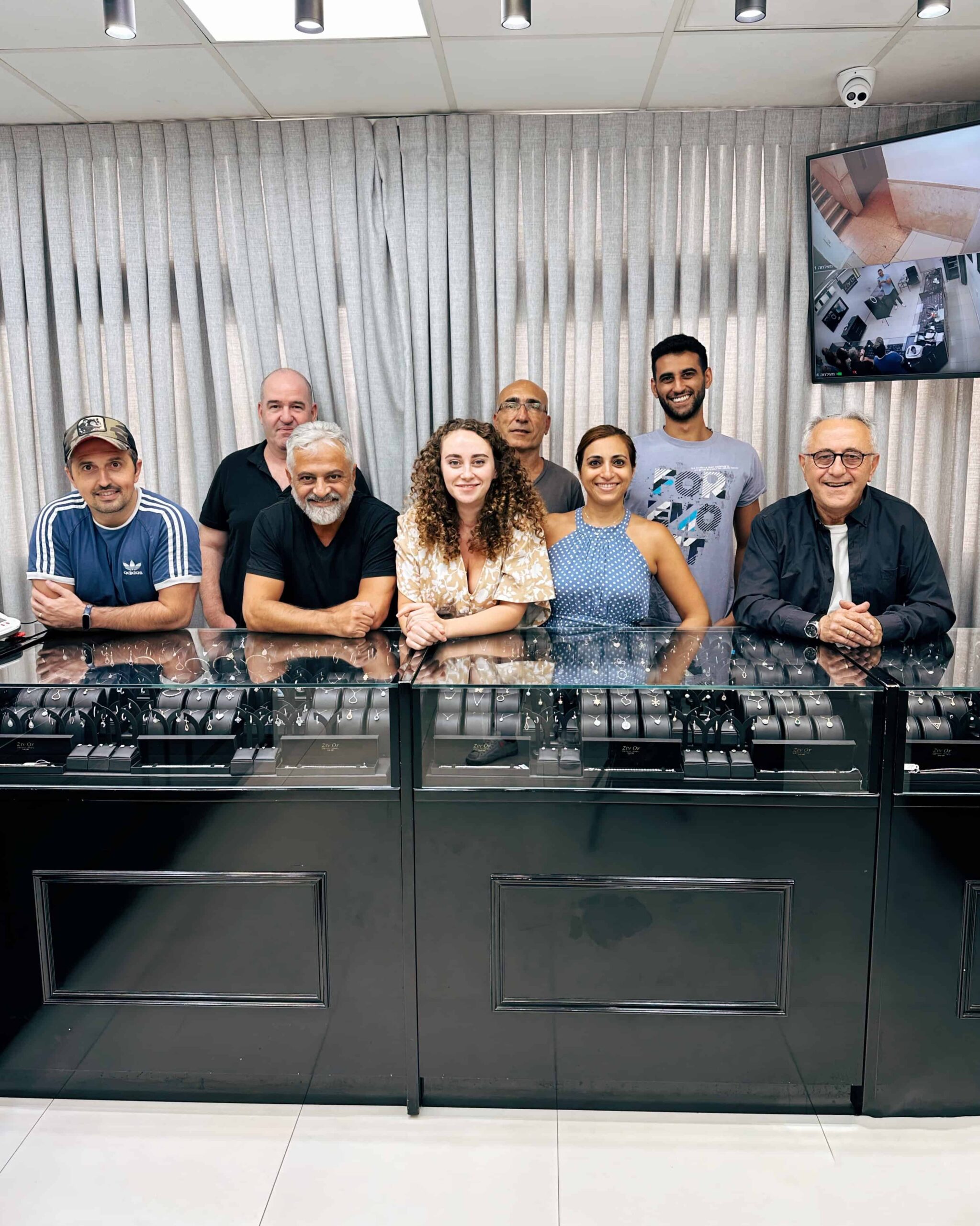 צוות חנות תכשיטים, גברים ונשים, עומדים מאחורי דלפק תצוגה של תכשיטים.
