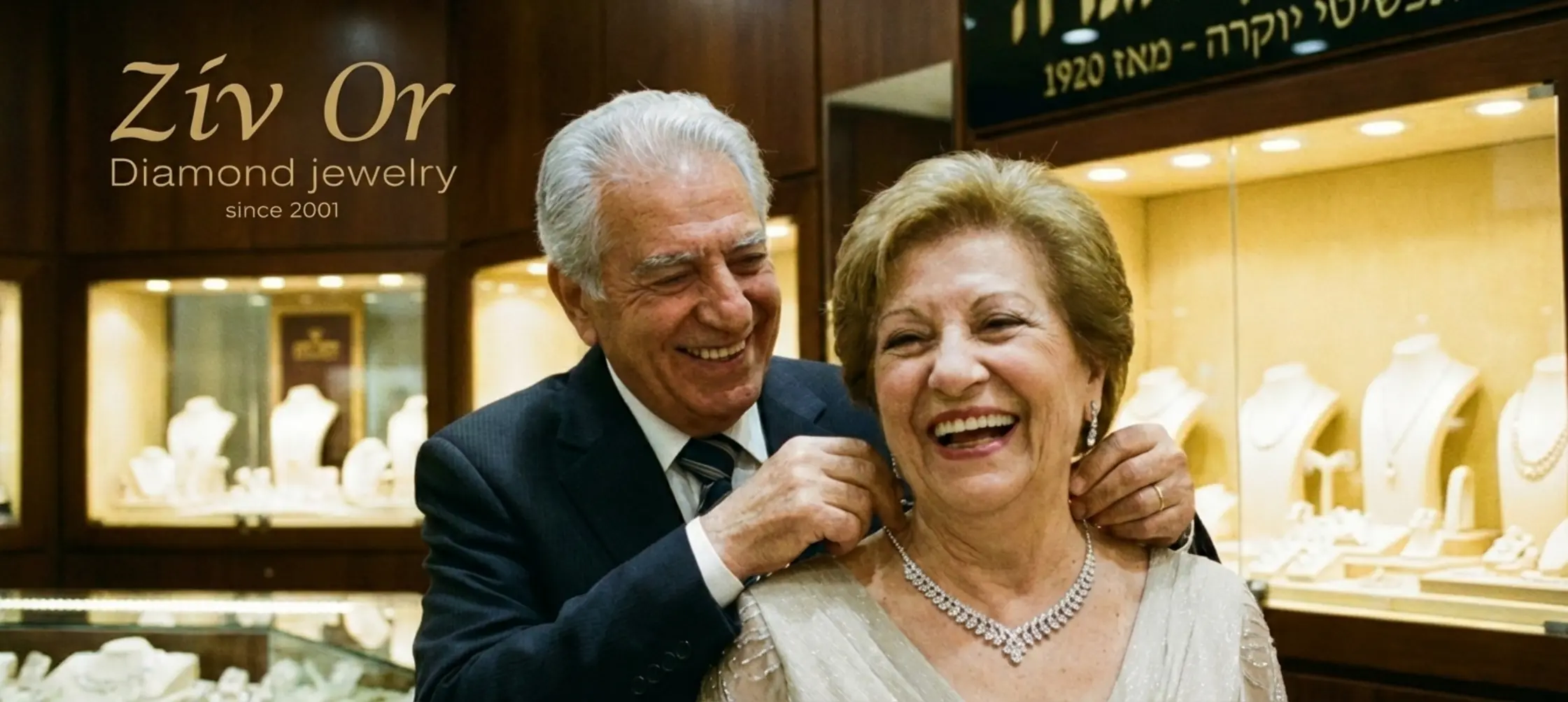 זוג מבוגר ומאושר מחייך בחנות תכשיטים יוקרתית כאשר הבעל עונד לאשתו שרשרת יהלומים נוצצת וברקע רואים תצוגת תכשיטים מוארת