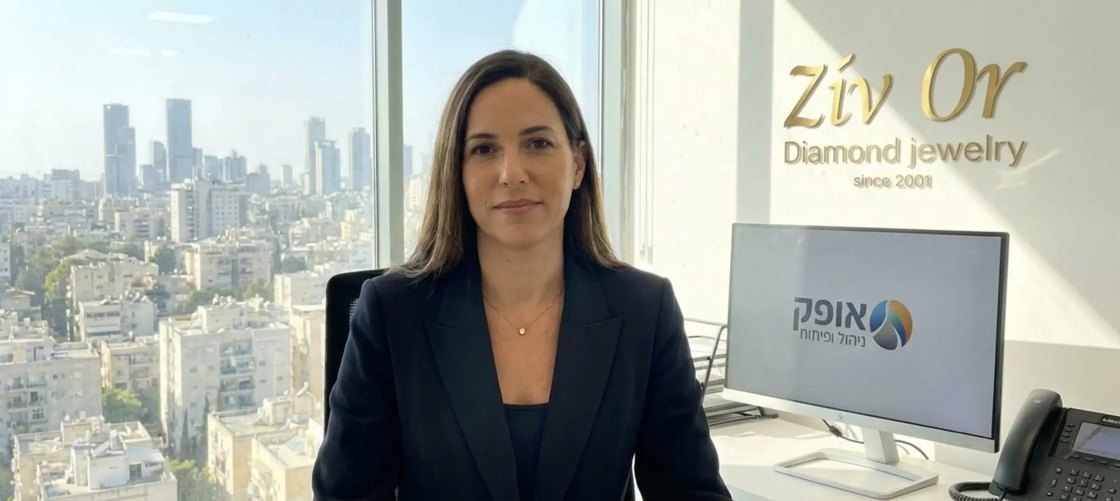 אישה מנהלת לבושה בבלייזר כהה, עונדת שרשרת זהב עדינה עם תליון יהלום קטן וטבעת סוליטר, יושבת במשרד מואר עם חלונות זכוכית גדולים המשקיפים לנוף עירוני