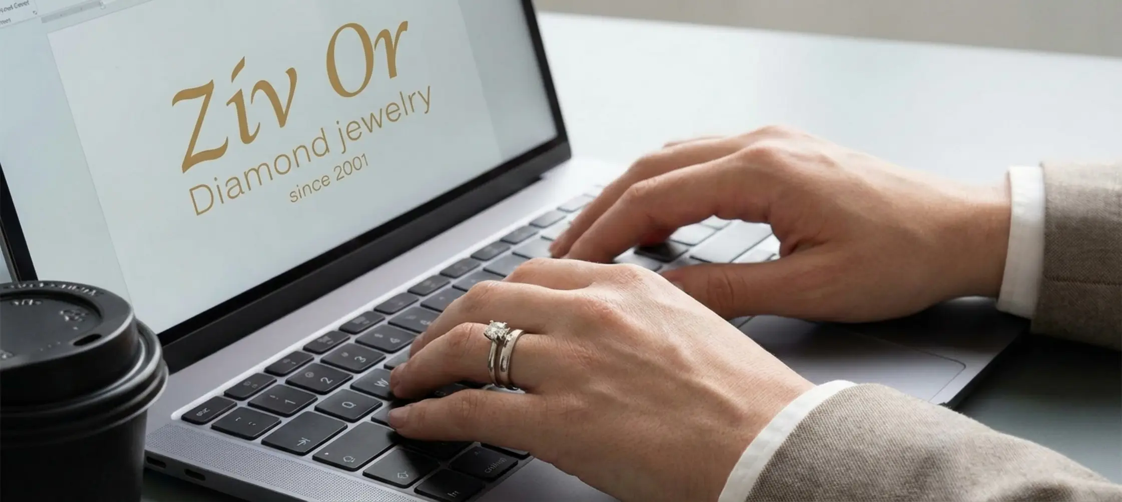 תקריב של ידיים מטופחות המקלידות על מקלדת מחשב נייד, על האצבע טבעת אירוסין קלאסית מזהב לבן לצד טבעת נישואין חלקה, משדרות יוקרה מאופקת וסמכותיות