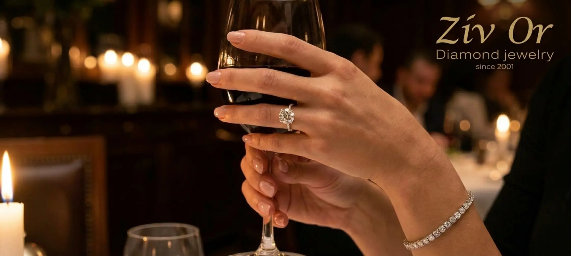 תקריב של ידיים נשיות אוחזות בכוס יין במסעדה יוקרתית עם תאורה עמומה, על האצבע טבעת יהלום מרשימה בגודל קראט אחד ועל פרק כף היד צמיד טניס נוצץ