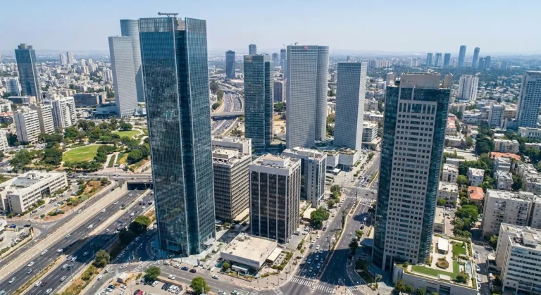 נוף אווירי של תל אביב מציג גורדי שחקים מודרניים, כבישים סואנים ופארק ירוק תחת שמיים בהירים.